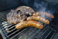 Steaks and sausage cooking and smoking food on an outdoor grill Royalty Free Stock Photo
