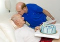 Son delivering a tender forehead kiss after reading a birthday card to his father on his father`s 89th birthday.