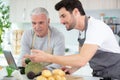 son with senior father with tablet in kitchen