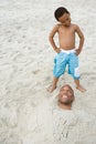Son looking at father buried in sand Royalty Free Stock Photo