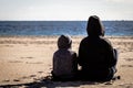 Son and mother sitting turn back on the beach and looking at the sea