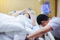 The son is taking care of the sick mother on the hospital bed. The boy is massaging his mother`s legs. female patients lying in