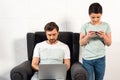 Son using smartphone and father using laptop