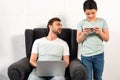 Son using smartphone and father using laptop