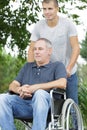 Son walking with disabled father in wheelchair at park Royalty Free Stock Photo