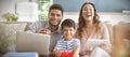 Son watching television while father and mother using laptop and digital tablet at home Royalty Free Stock Photo