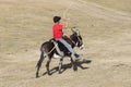 Song Kul, Kyrgyzstan, August 8 2018: A boy in a red T-shirt rides a donkey through the steppe at Song Kul Lake in Kyrgyzstan