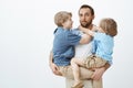 Sons are taking advantage of loving and caring father. Portrait of clueless funny european dad holding children on hands