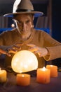 Soothsayer using crystal ball to predict future at table in darkness with candles. Fortune telling Royalty Free Stock Photo