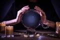 Soothsayer using crystal ball to predict future at table in darkness, closeup. Fortune telling Royalty Free Stock Photo