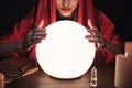 Soothsayer using glowing crystal ball to predict future  at table in darkness, closeup. Fortune telling Royalty Free Stock Photo