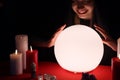 Soothsayer using glowing crystal ball to predict future at table in darkness. Fortune telling Royalty Free Stock Photo