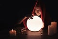 Soothsayer using glowing crystal ball to predict future at table in darkness, space for text. Fortune telling Royalty Free Stock Photo