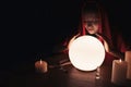 Soothsayer using glowing crystal ball to predict future at table in darkness, space for text. Fortune telling Royalty Free Stock Photo