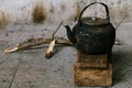 Sooty old teapot on small wooden bench in open kitchen