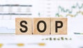 SOP or Standard Operating Procedure - acronym on wooden cubes on a financil background. Business concept