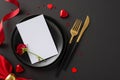 Elegant table top view featuring fine plates, menu card, cutlery, delectable chocolates, rose, luxurious ribbon on black surface Royalty Free Stock Photo