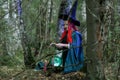 The sorceress in a hat and a black cloak in the forest charms over a luminous crystal ball. Horizontal photo