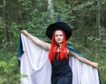 The sorceress in a hat and a black cloak in the forest divides over the sorceress with red hair in a hat and a black