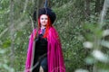 A sorceress with red hair in a hat and a purple cloak in the forest in her hand with a burning candle.