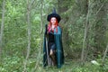 A sorceress with red hair in a pointed hat and a black cloak in the forest is engaged in charms with a candle.