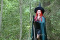 A sorceress with red hair in a pointed hat and a black cloak in the forest is engaged in charms with a candle. Royalty Free Stock Photo