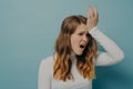 Sorrorful stressed young woman holding hand on head isolated over blue studio wall