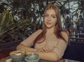 Sorrowful young lady is sitting in cafe, coffee cup is served on table in front of her