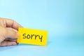 Sorry message concept. Hand holding a bright yellow paper with written message note. Royalty Free Stock Photo