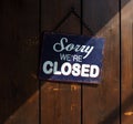 Sorry we`re closed, blue and white sign on old wooden door, with a shadow that divides it into a clear and dark part