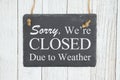 Sorry we`re Closed Due to weather text on a hanging chalkboard on weathered whitewash textured wood