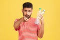 Sort your rubbish! Serious bearded man in striped t-shirt holding plastic bottle and pointing finger at camera, worrying about