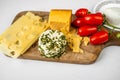 Sorts of cheese sliced, hard, white with herbs and tomato on wooden kitchen board, closeup Royalty Free Stock Photo