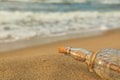 SOS message in glass bottle on sand near sea, closeup. Space for text Royalty Free Stock Photo