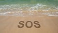 SOS message written in the sand on a beach with waves coming in. Concept for emergency, help, or danger Royalty Free Stock Photo