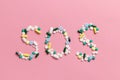 SOS sign made of pills and capsules on a pink background. The concept of illness and drug addiction. Suicide. Death from