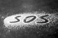 SOS word hand written on white powder, distress signal
