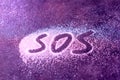 SOS word hand written on white powder, distress signal