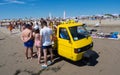 Fruit seller with yellow vehicle on three wheels on the beach.