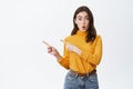 Sounds cool. Intrigued and excited young woman pointing fingers left, say wow and staring at camera impressed, standing Royalty Free Stock Photo