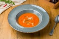 Soup cream of tomato on grey plate with greens on wooden table