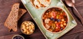 Soup with meat in bowl with oregano, chickpeas, peppers and vegetables served with crackers and bread on dark wooden background, Royalty Free Stock Photo