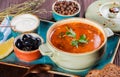 Soup with meat, olives, herbs, lemon, sour cream in bowl, black bread and spices on dark wooden background, homemade food.