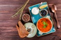 Soup with meat, olives, herbs, lemon, sour cream in bowl, black bread and spices on dark wooden background, homemade food