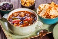 Soup with meat, oregano, chickpeas, peppers and vegetables served with crackers and bread on plate on dark wooden background.