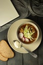 Soup with meat, radishes and cabbage on a plate. Next to a spoonful of sour cream are two slices of bread, a notebook