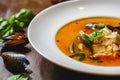 Soup with mussels and vegetables in white plate on wooden table Royalty Free Stock Photo