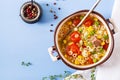 Soup with small pasta, vegetables and pieces of meat in bowl on blue table.