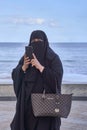Elderly muslim arab woman in black nikab and abaya with a handbag with the emblem of louis vuitton talks on the mobilephone
