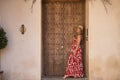 South American woman, young, beautiful, blonde with flower dress, sunglasses and hat, leaning against a wooden door frame, pensive